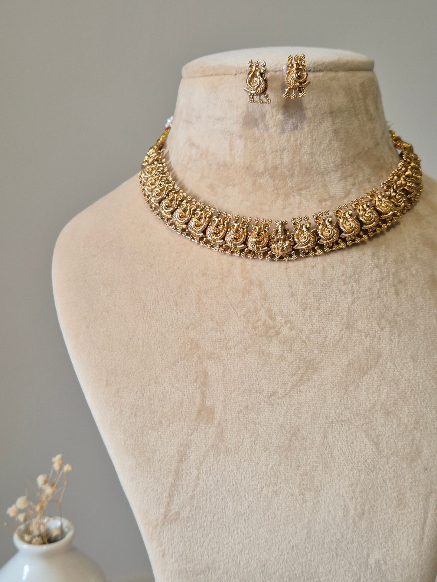 Gold necklace set, Bhaviki by Naitri, ethnic design displayed on fabric.