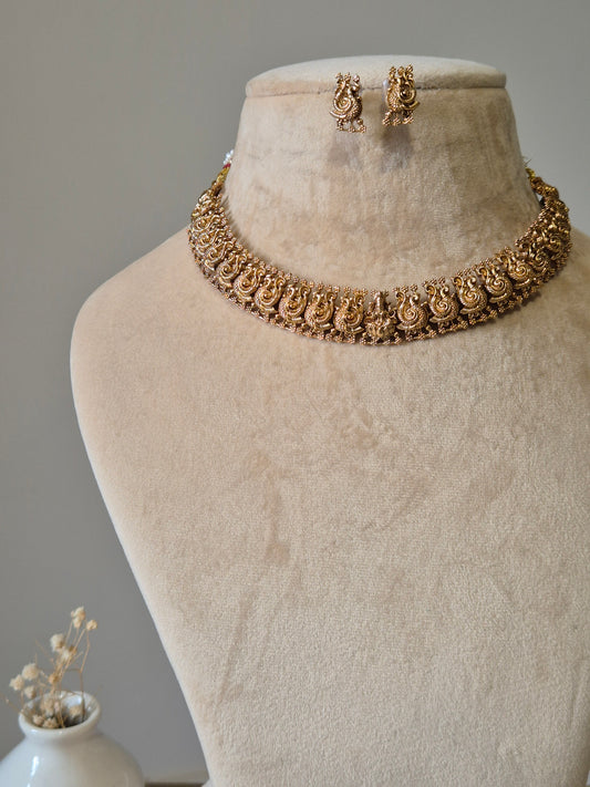 Gold necklace set, Bhaviki by Naitri, ethnic design displayed on fabric.