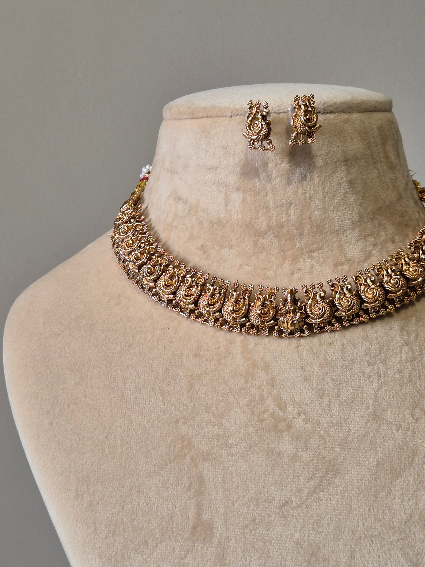 Gold necklace set, Bhaviki by Naitri, ethnic design displayed on fabric.