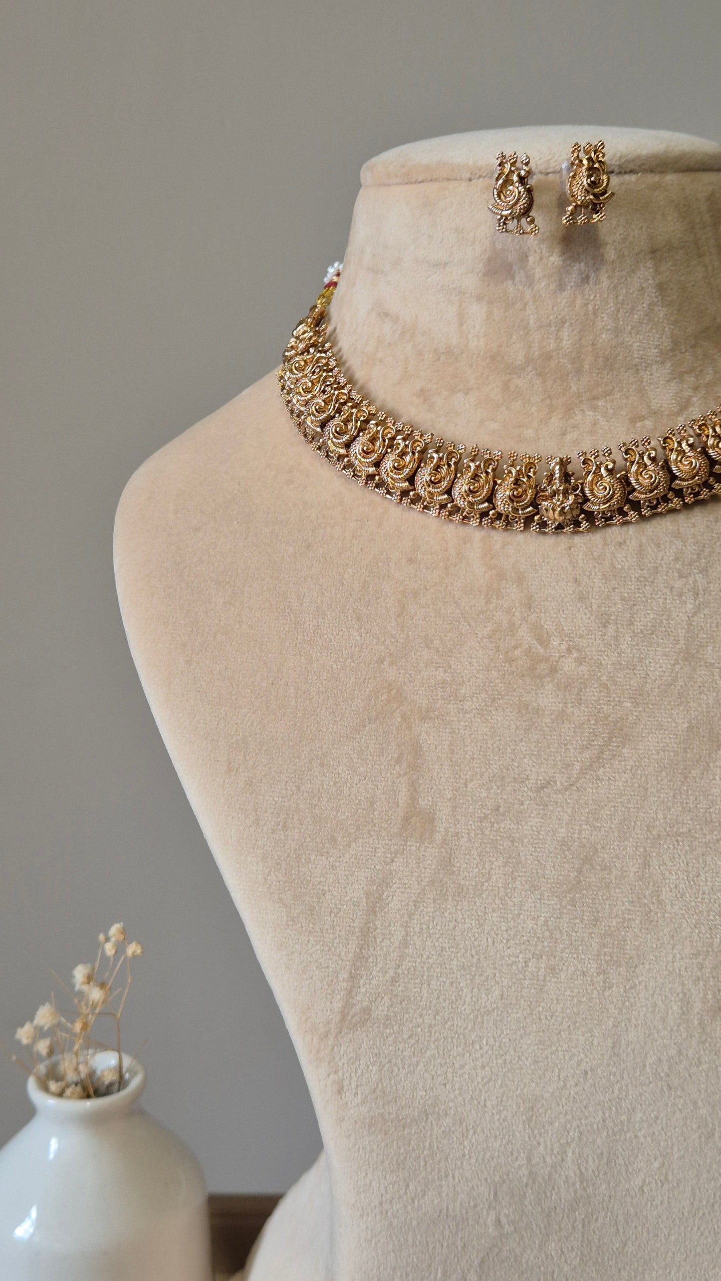 Gold necklace set, Bhaviki by Naitri, ethnic design displayed on fabric.