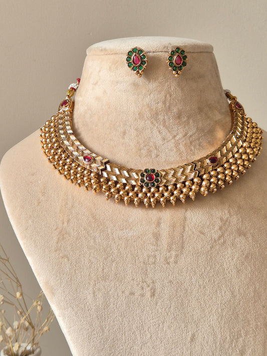 Statement gold necklace set with red accents, Trishani by Naitri, displayed flat.