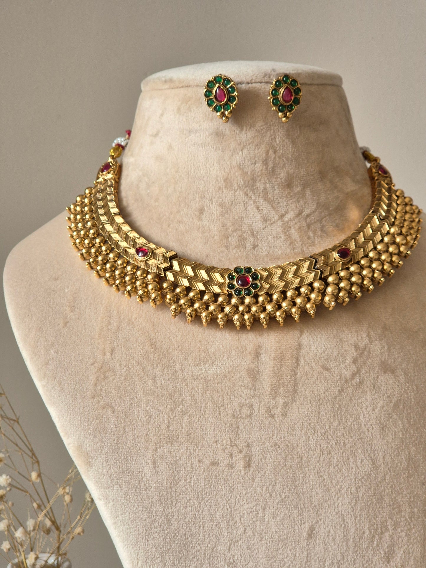 Statement gold necklace set with red accents, Trishani by Naitri, displayed flat.