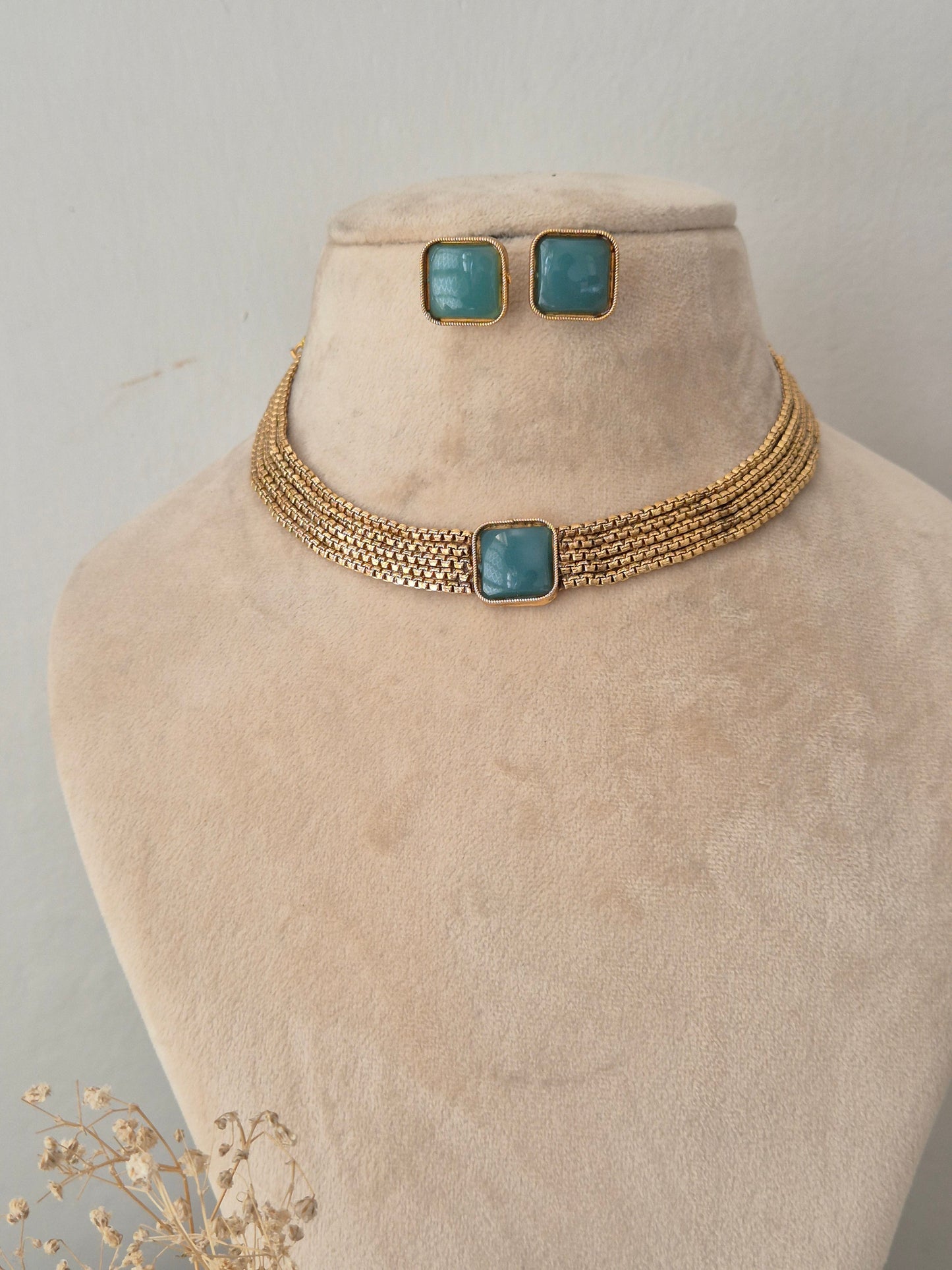 Multi-strand woven gold collar necklace with a central square teal stone and matching stud earrings