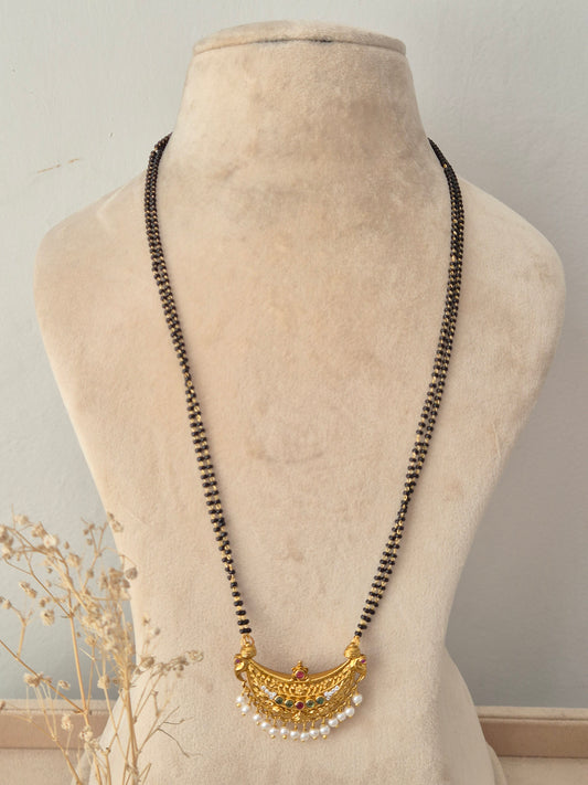 Padmini Mangalsutra with fine double-stranded black beads and a semi-circular gold pendant detailed with intricate filigree work, red and green gemstone accents, and hanging pearl beads