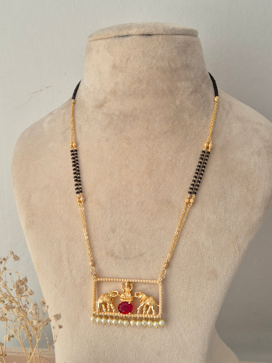Jivinta Mangalsutra featuring a fine black-and-gold beaded chain attached to a gold rectangular frame pendant with twin elephant motifs flanking a central oval red stone, finished with hanging white pearls