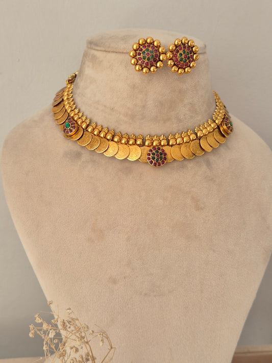 Traditional temple jewellery choker set featuring a gold-toned coin necklace studded with ruby-red and green stones, paired with coordinating round floral stud earrings