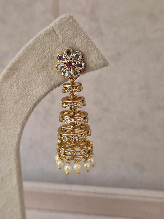 Gold-toned tiered jhumka earring with a floral stud top set with clear and ruby-pink stones, dangling pearl beads