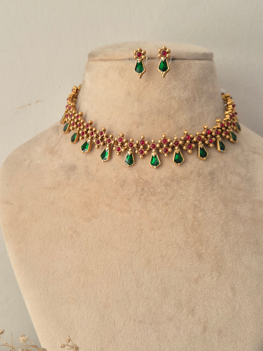 Traditional Indian antique gold choker necklace featuring a row of ruby-red stones embellished with dangling emerald-green teardrop stones, complete with coordinating small drop earrings