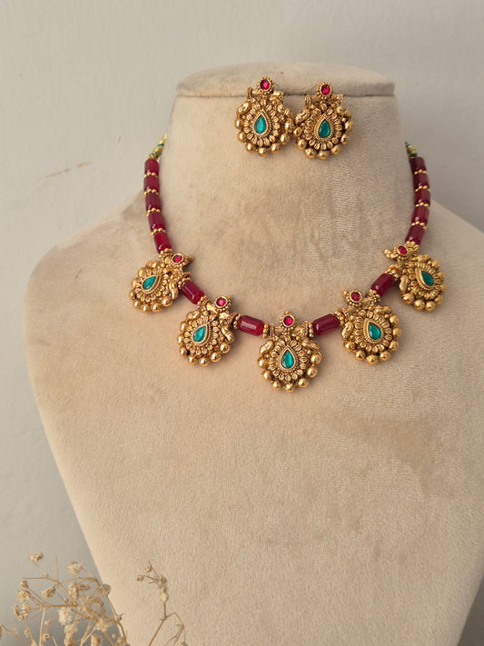 Traditional Indian antique gold jewellery set featuring a necklace of faceted ruby-red beads strung with ornate gold pendants containing teardrop turquoise-green stones