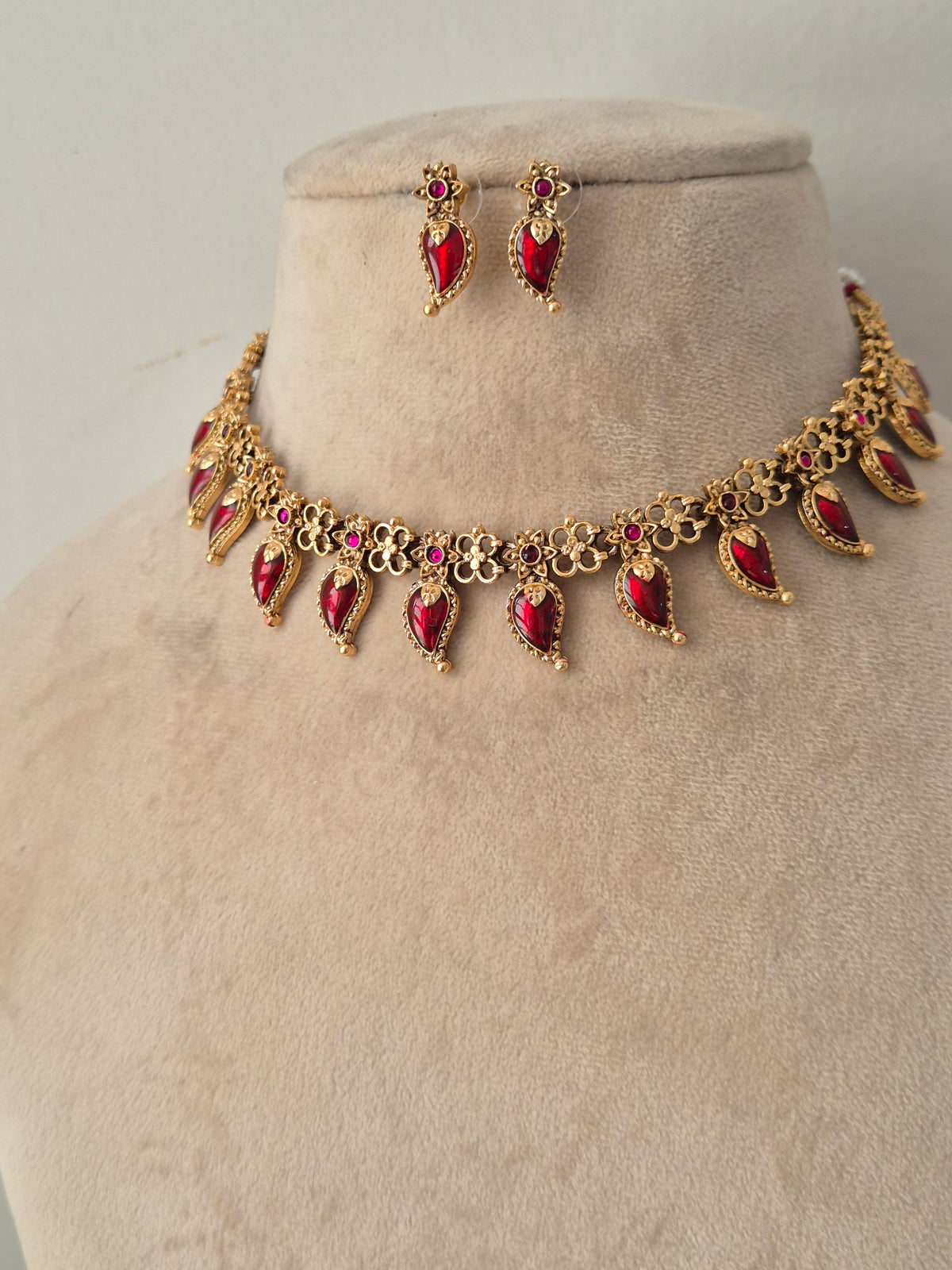 Traditional gold-toned choker with ruby-red stone dangles and matching drop earrings on a display bust