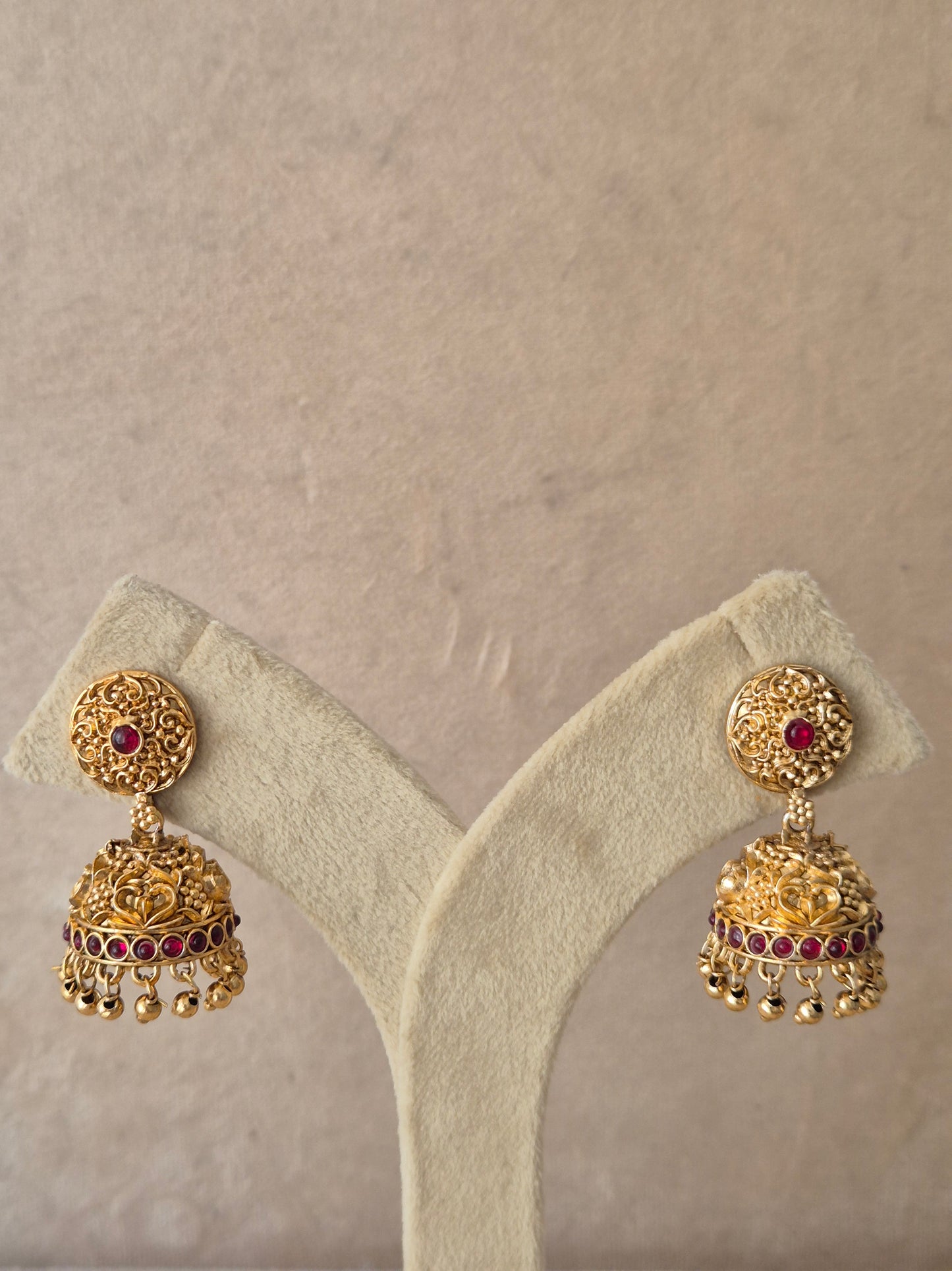 Gold-plated Jhumki earrings with red stones and hanging bead details raditional gold-plated Jhumka earrings with red gemstones and bead dangles by naitri.in
