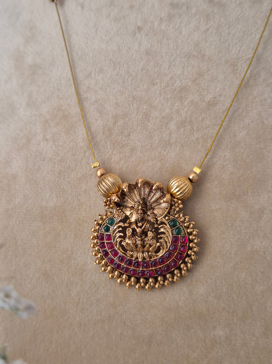 Minimalist invisible chain necklace with a textured gold-polished pendant and red-green stone embellishments, paired with matching red and gold earrings for a modern Indian aesthetic by naitri.in