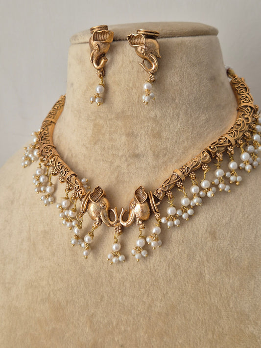 Traditional Indian ethnic jewelry set showing a brass alloy gold-toned necklace with clustered pearl embellishments and matching hanging earrings by naitri.in