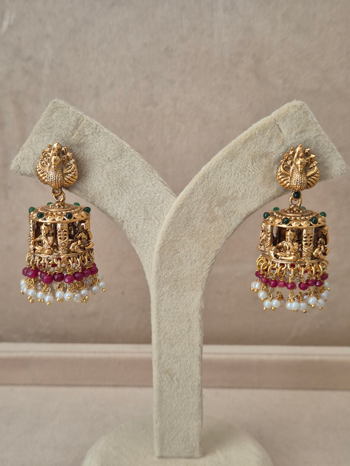 Traditional gold-toned peacock design Jhumka earrings with pink gemstones and white pearl drops by naitri.in