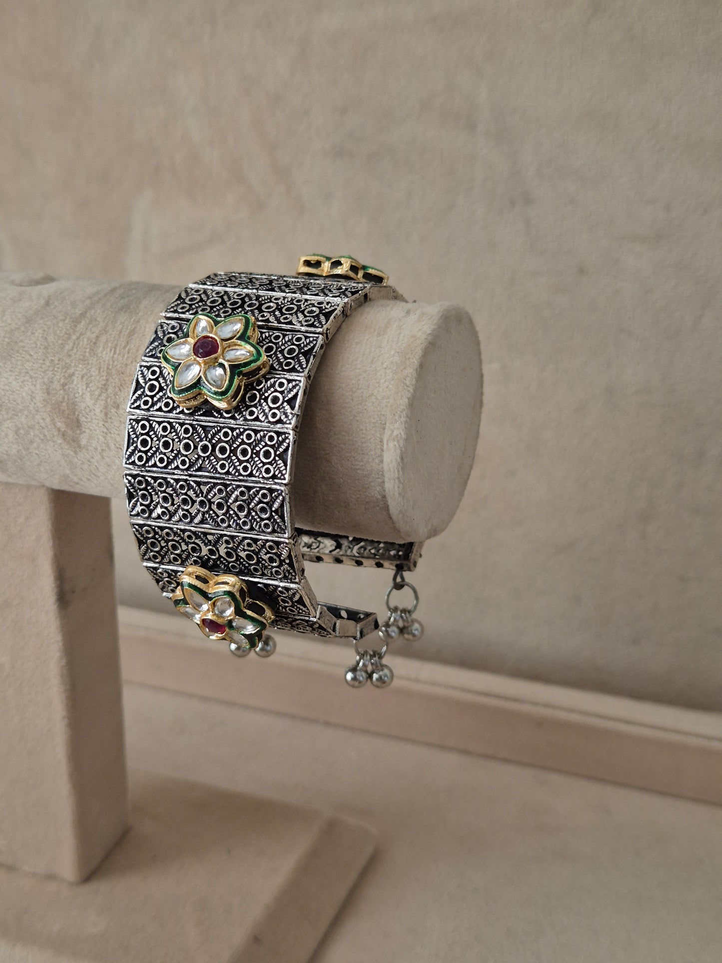 Wide oxidized silver Bharti cuff bangle with geometric cutout patterns and dangling ghungroo accents. by naitri.in