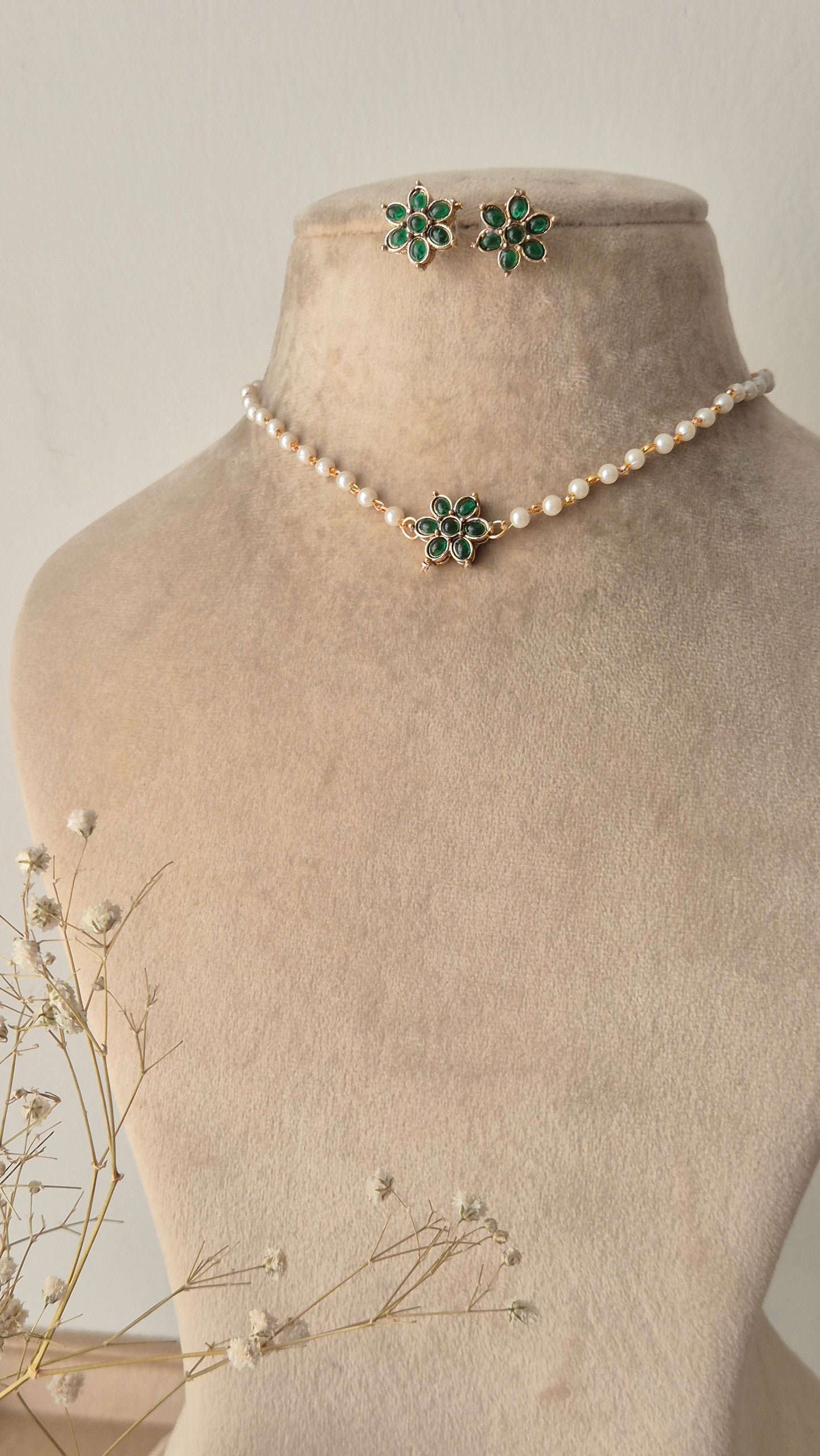 Pearl choker necklace with a green stone floral pendant, A delicate pearl strand choker featuring a central gold-plated floral motif with green stones by naitri.in