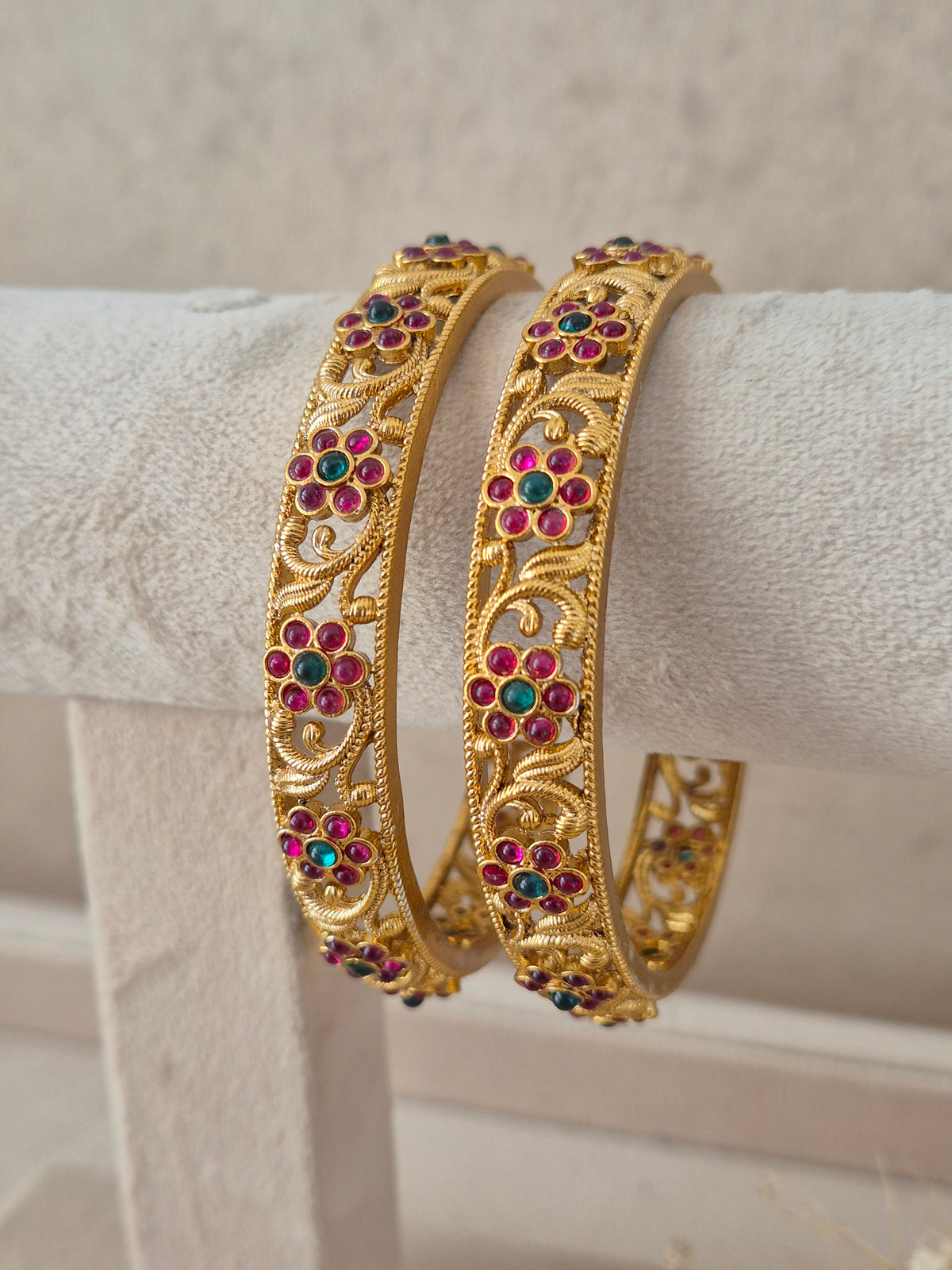 Festive Indian gold-plated bangles embellished with vibrant red and green floral stone crafting for weddings and special occasions by naitri.in