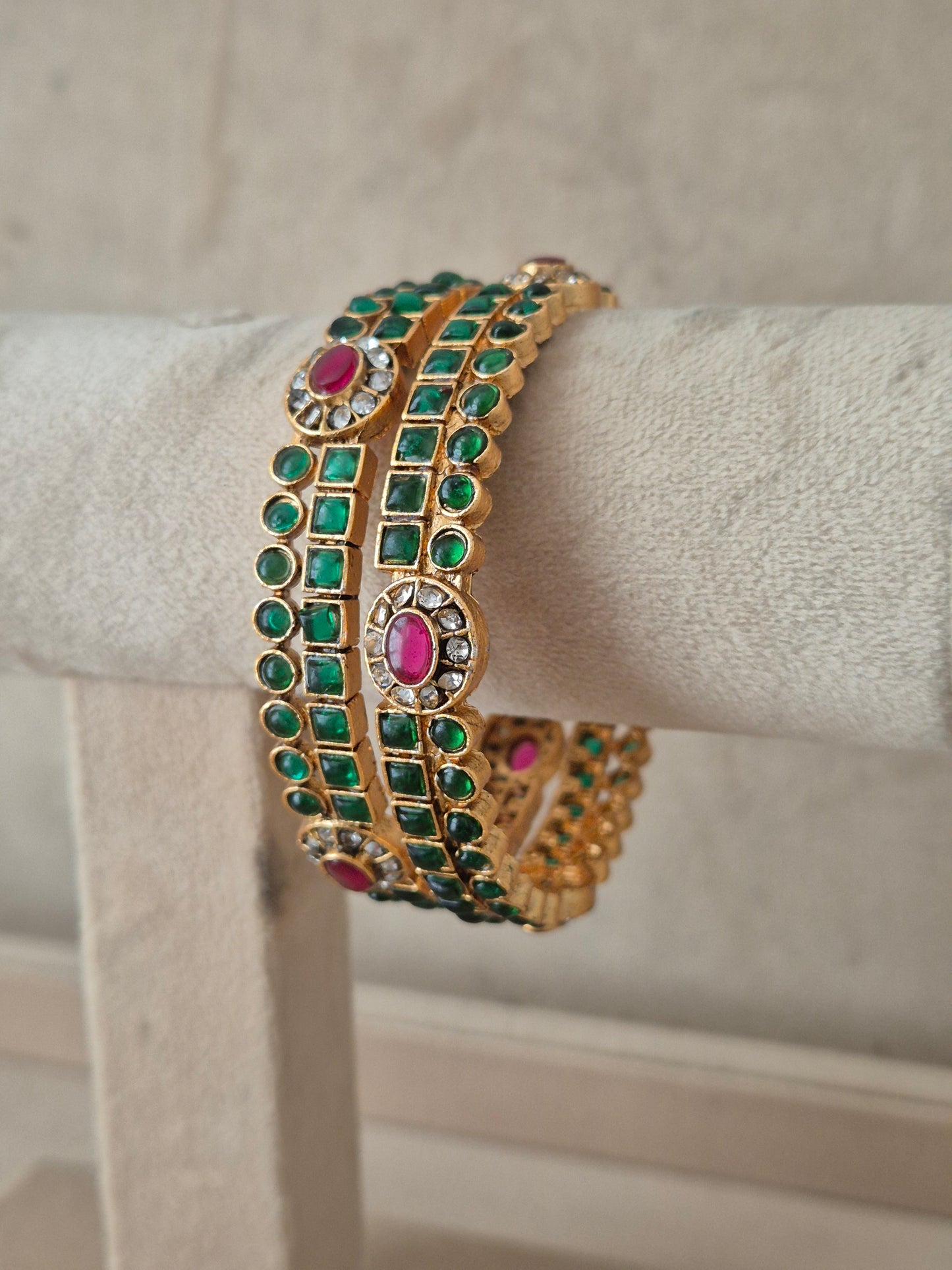 A gold-plated Indian style bangle bracelet with rows of green square-cut stones and pink oval stones, by naitriin