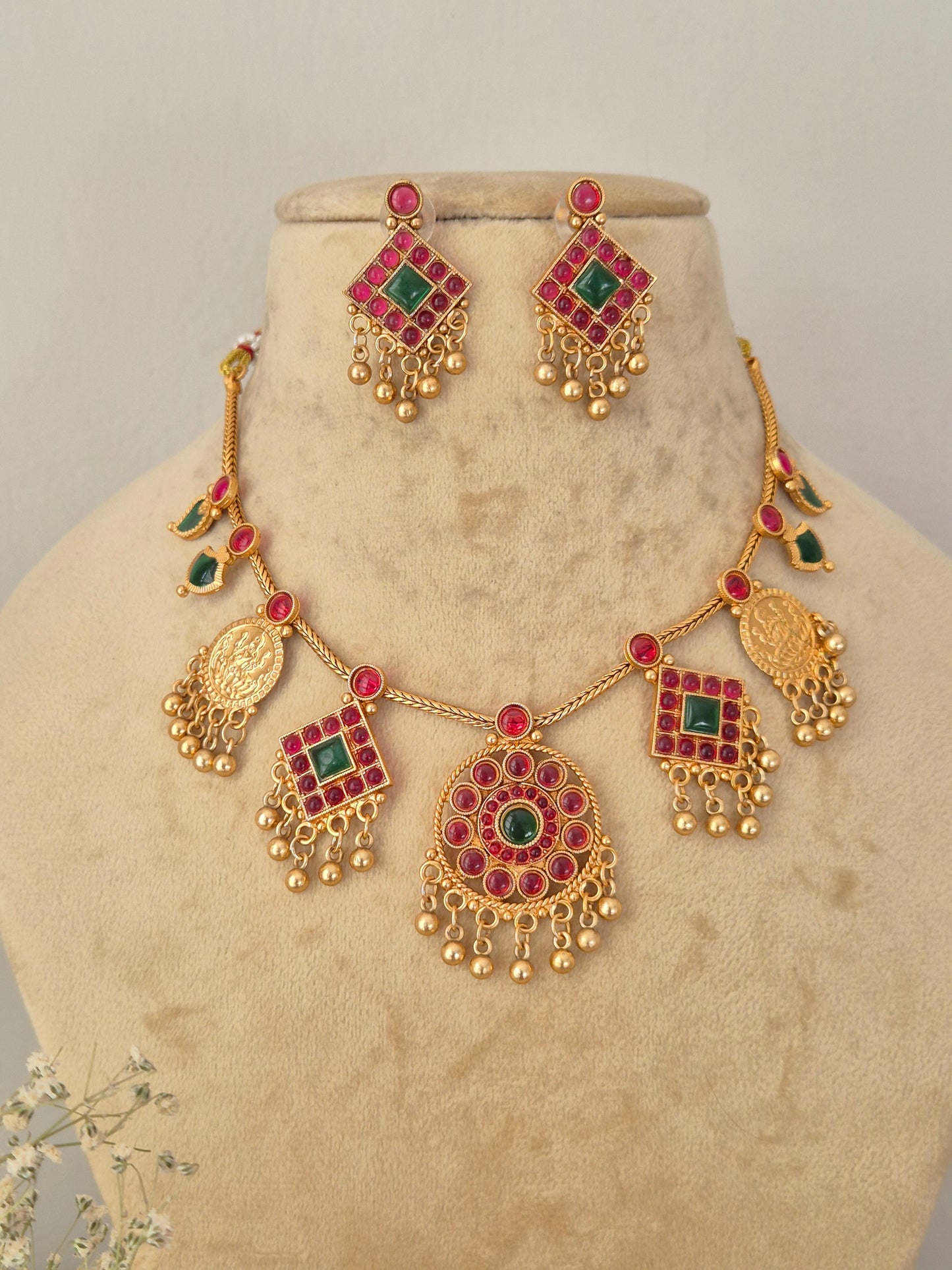Gold-toned traditional Indian jewelry set featuring a necklace and matching earrings with red and green stone accents, for festive wear by naitri.in