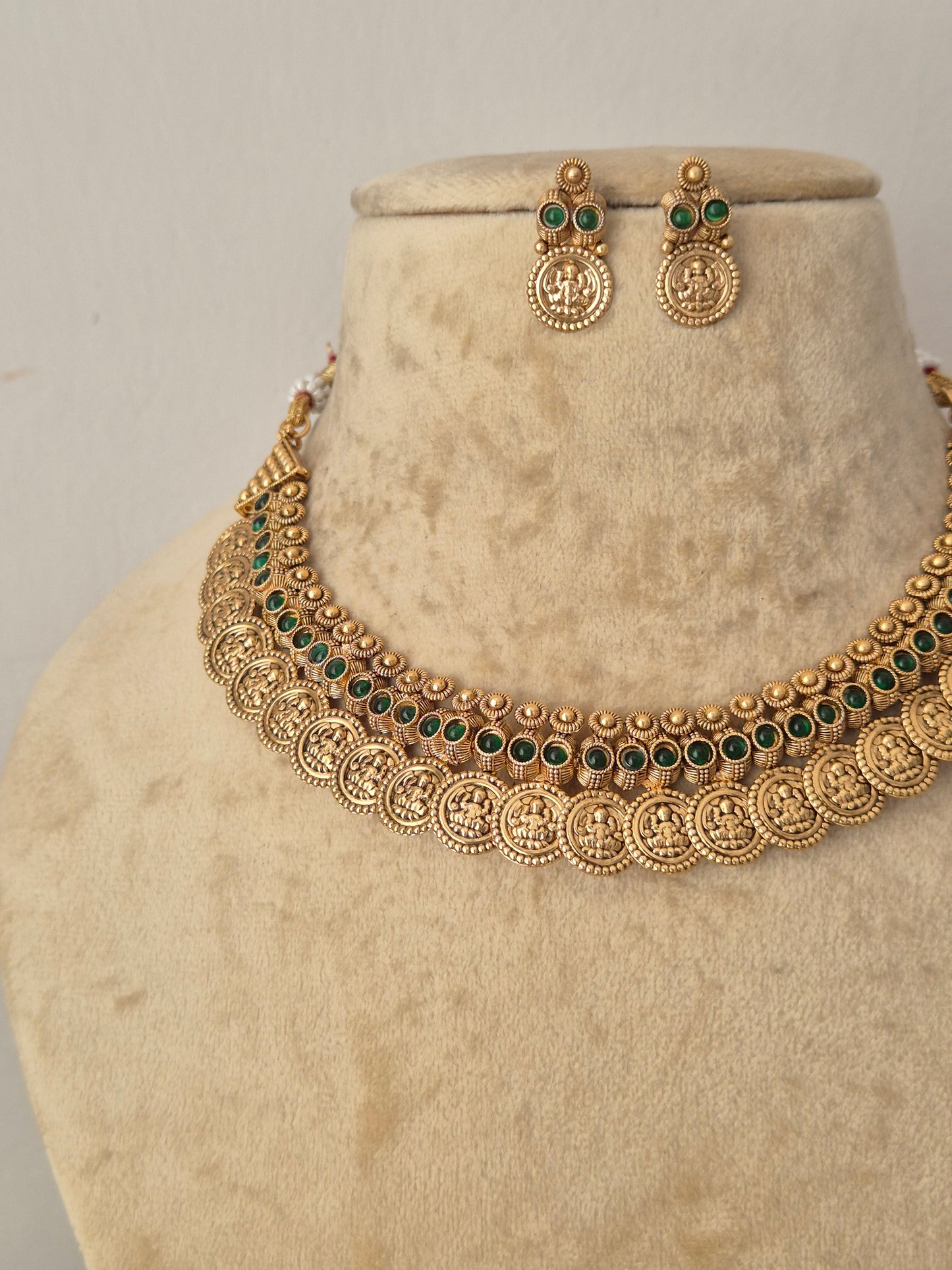 Gold-toned traditional necklace and matching earrings features circular coin-like motifs with small dark green stone accents, and the matching earrings have similar round gold pendants with green stones by naitri.in
