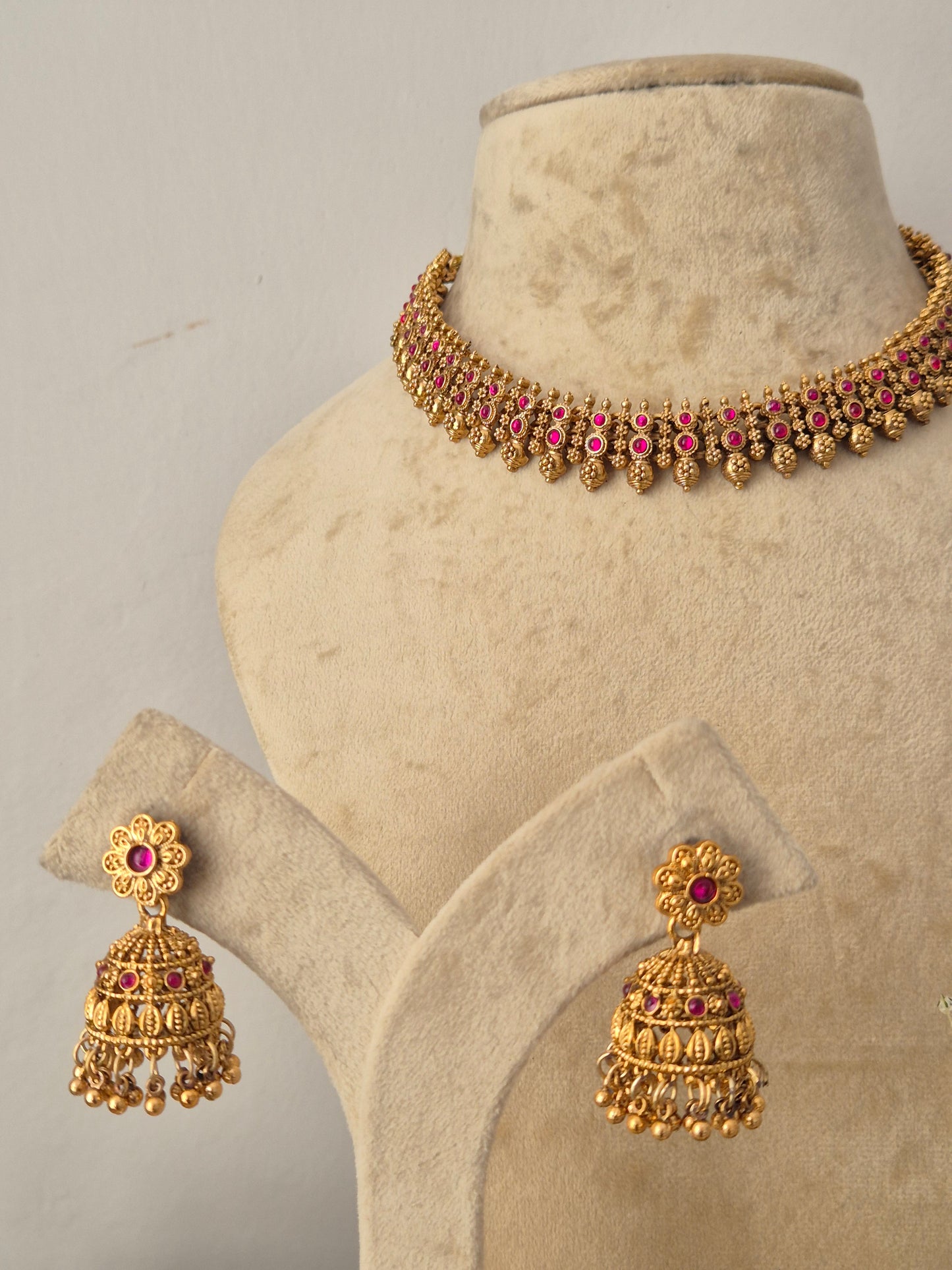 Traditional Indian gold-toned choker necklace and matching jhumka earrings embellished with deep pink gemstone accents, by naitri.in