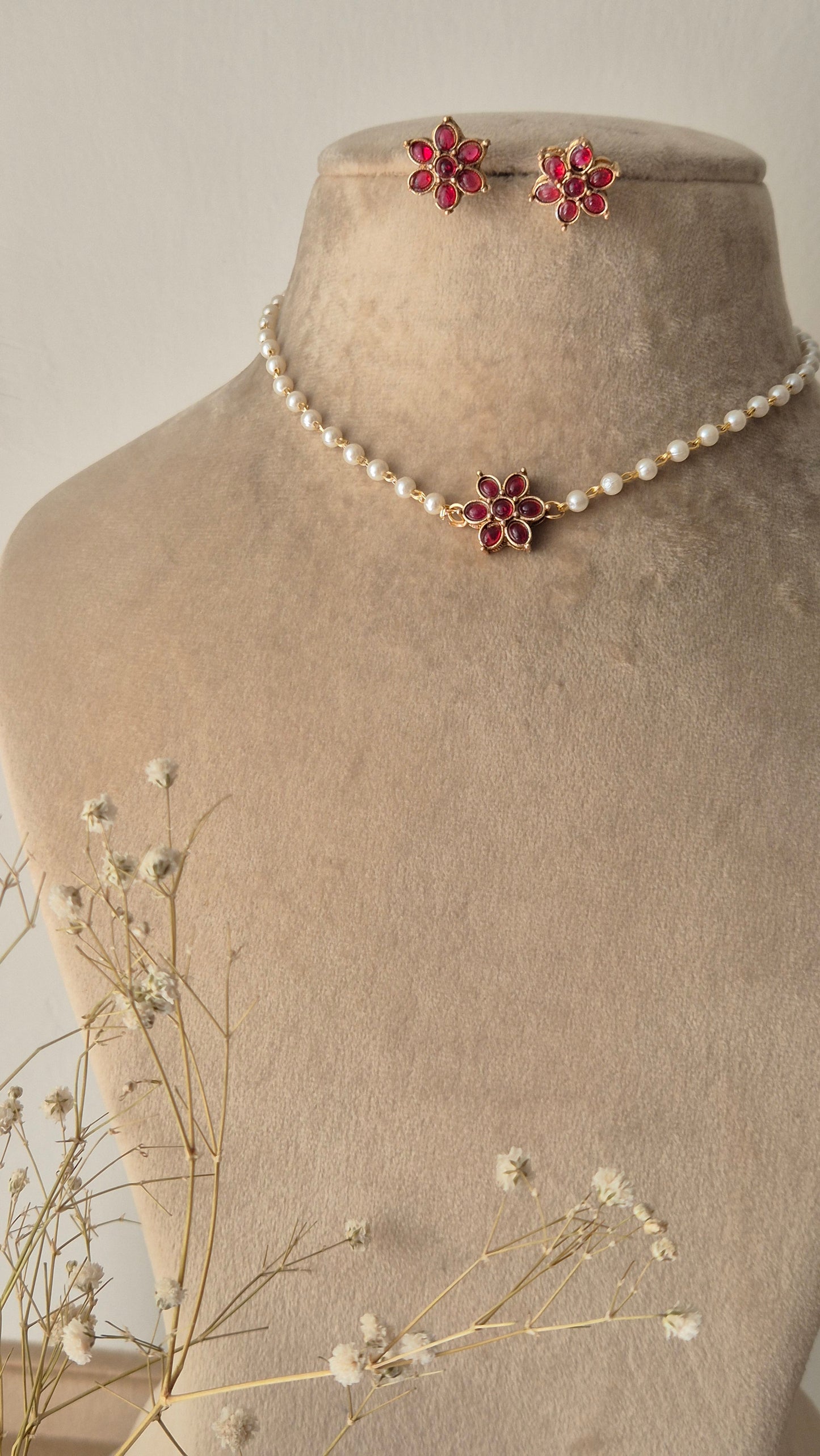 Pearl choker necklace with a pink stone floral pendant, A delicate pearl strand choker featuring a central gold-plated floral motif with pink stones by naitri.in