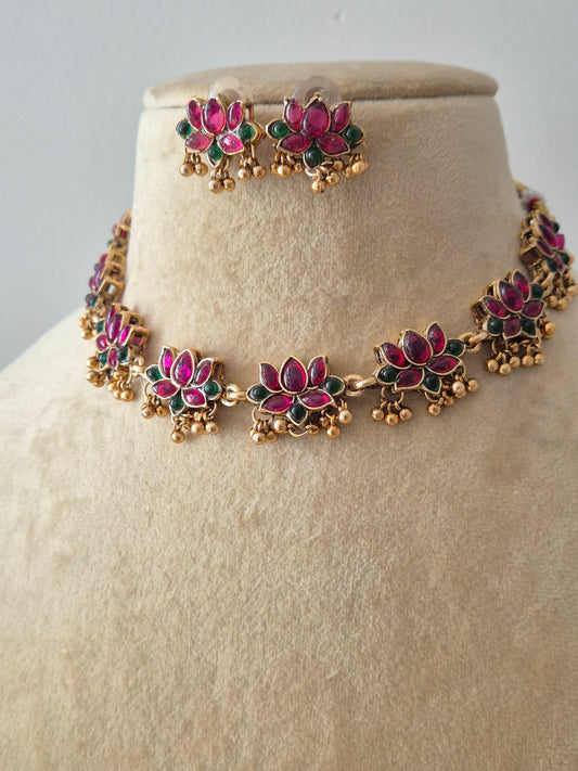 Handcrafted jewelry set in brass alloy with a polished golden finish, traditional lotus floral engravings, and vibrant red and green stone embellishments by naitri.in