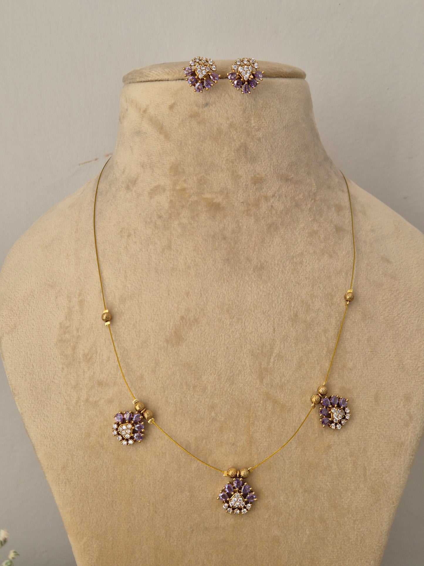 Modern Indian style delicate golden brass alloy necklace and earring set with purple stone embellishments from the NAITRI Jasmeet collection Handcrafted delicate gold chain choker set showcasing geometric crystal and purple stone floral drops by naitri.in