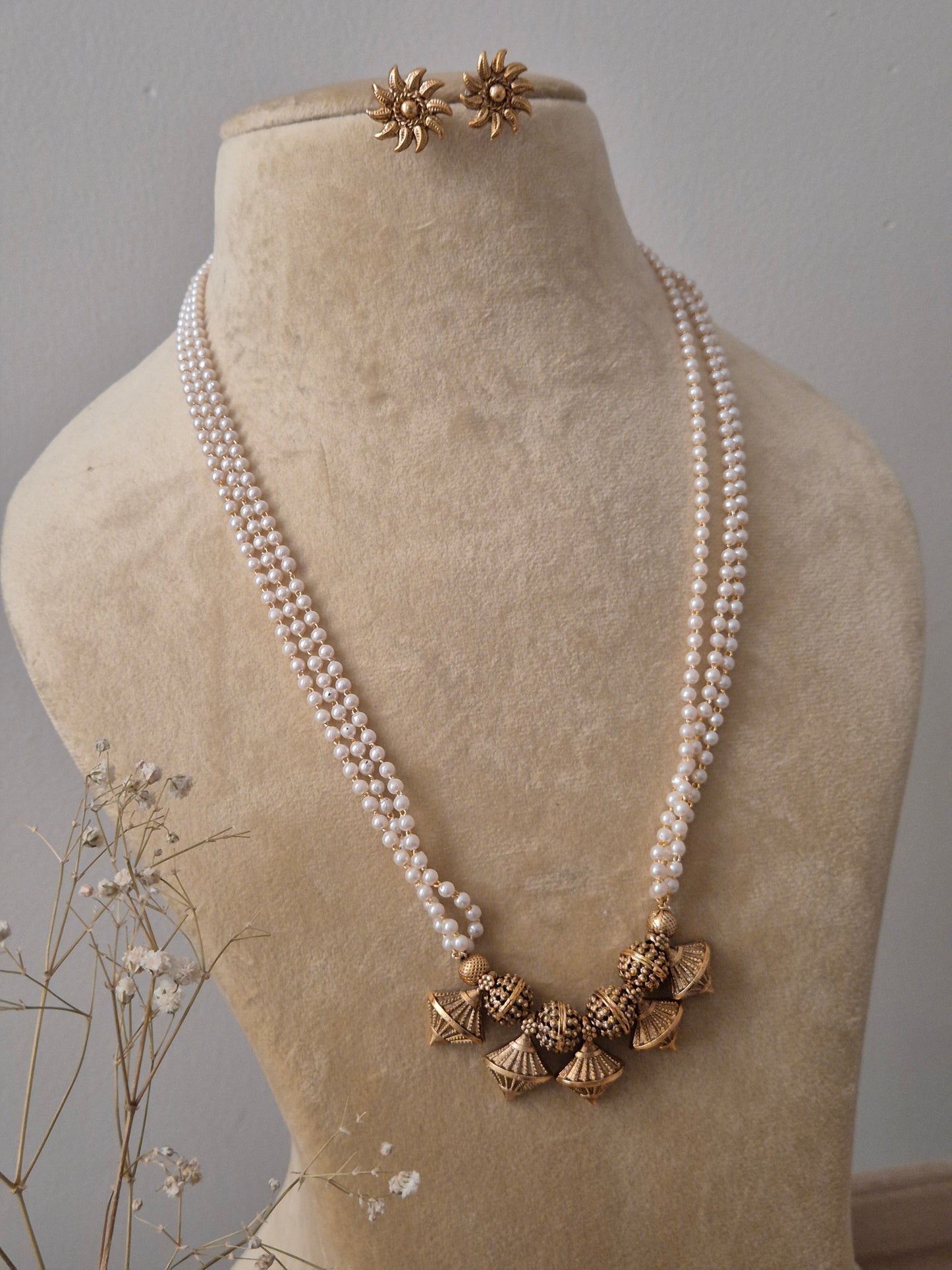 Gold-plated brass alloy jewelry set including a layered pearl necklace with metallic bell-shaped charms and intricate sunburst-style earrings by naitri.in