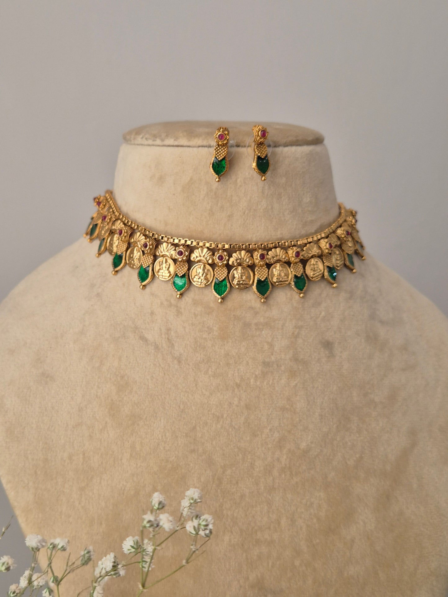traditional Indian bridal choker set in gold and green, handcrafted with floral motifs and stone drops, shown with baby's breath flowers in the foreground by naitri.in