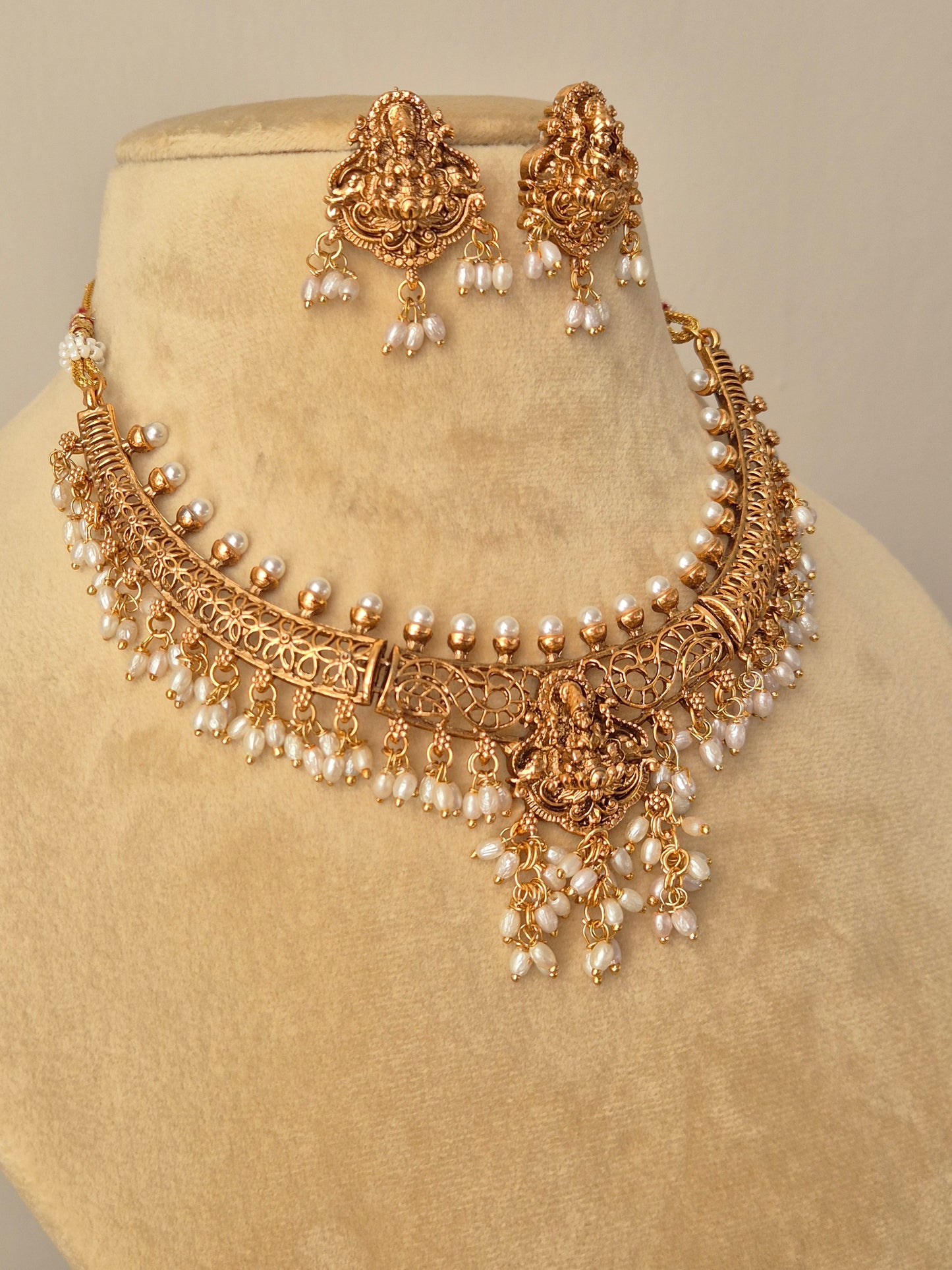Close-up of the Keshavi Necklace Set: a golden brass choker with a central Goddess pendant, multiple pearl hangings, and matching floral-deity stud earrings by naitri.in