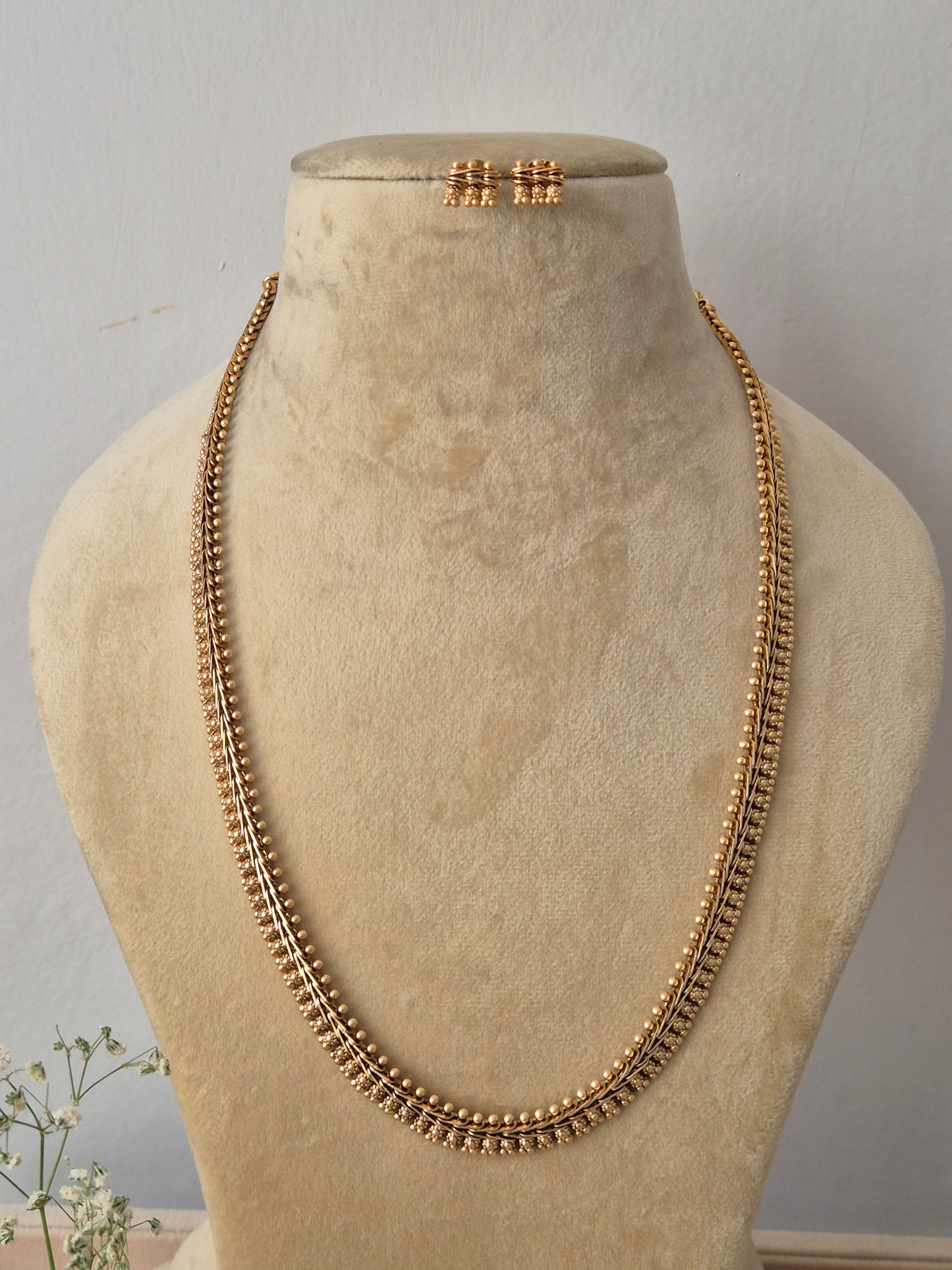 Long, opera-length gold-toned chain necklace featuring an intricate, multi-layered textured bead pattern along its edges, shown with coordinating round stud earrings by naitri.in