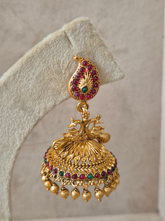 Handcrafted earrings in brass alloy with a polished golden finish and vibrant red and green stone embellishments by naitri.in