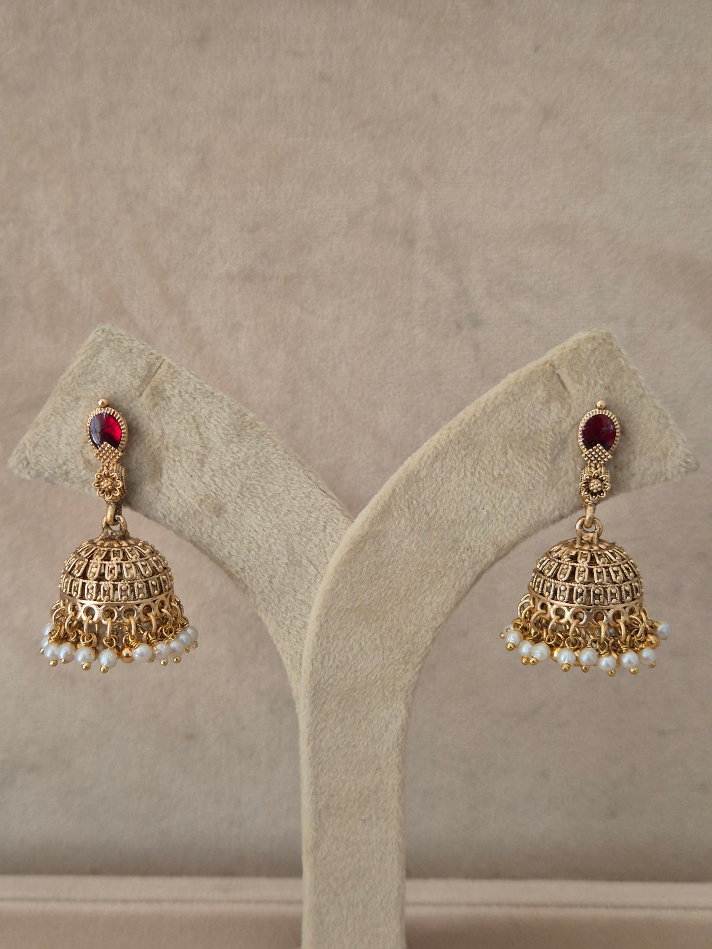Traditional gold-plated Jhumka earrings with a red gemstone stud and tiny white pearl drops by naitri.in
