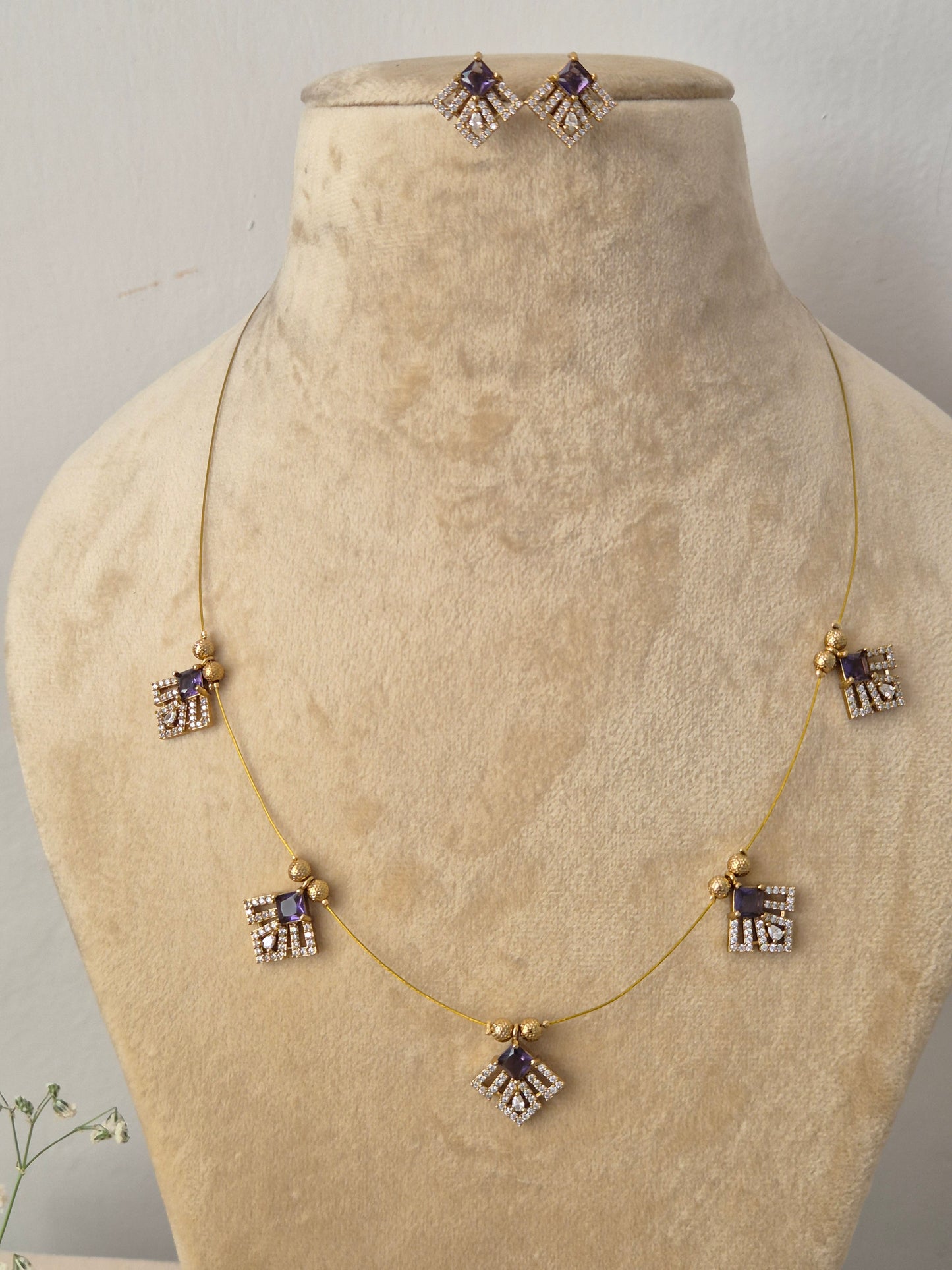 Modern Indian style gold chain necklace set with purple stone embellishments. Handcrafted delicate gold pendant necklace and earring set showcasing geometric crystal charms by naitri.in