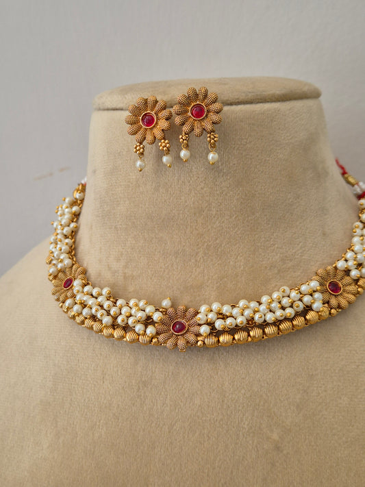 Handcrafted brass alloy choker made of intricate pearl strands and ruby-red floral embellishments, delicate gold flowers by naitri.in