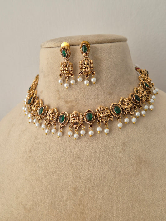 Antique gold-plated ethnic choker set featuring intricate Indian artisanal metalwork, oval-cut green stones, and delicate hanging white pearls, shown alongside matching dangle earrings. by naitri.in