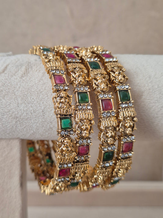 Close-up of Naitri Ashika premium gold ethnic bangle set with traditional Indian floral metalwork and vibrant red and green stone accents by naitri.in