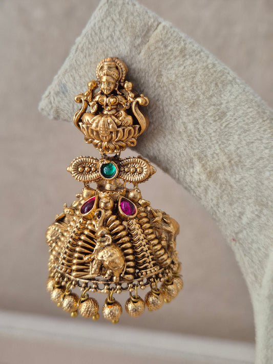 Pair of antique gold-finish jhumka earrings featuring traditional goddess motifs on the stud, green and ruby stone highlights, and delicate bell drops by naitri.i