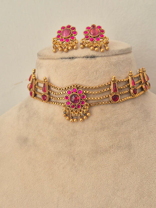 Antique gold-toned choker necklace showcasing an intricate metallic floral band, vibrant pink stone clusters, and delicate hanging gold bead drops, shown with coordinating round stud earrings by naitri.in