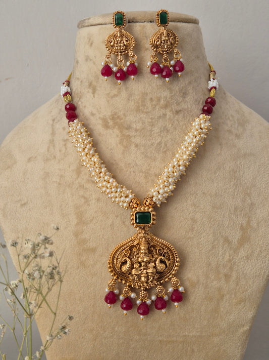 Gold-plated traditional Indian jewelry set featuring a necklace and matching earrings with cream-colored faux pearls, green stone accents, and deep red bead drops, by naitri.in