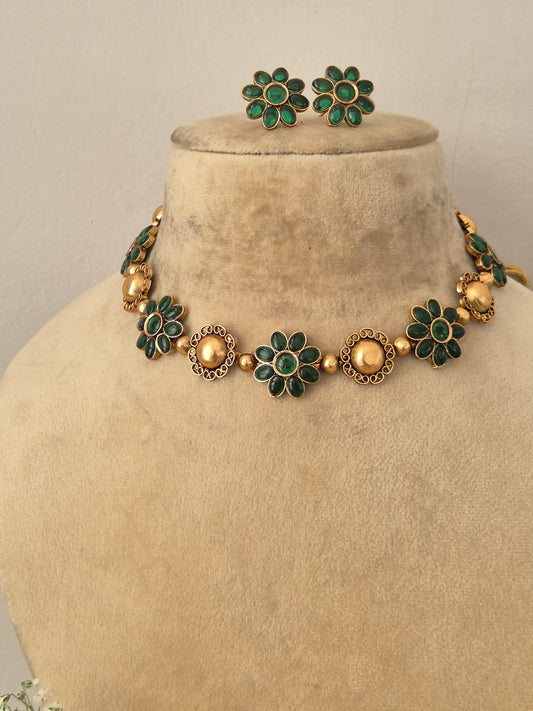 Modern Indian ethnic imitation jewelry set including a golden brass alloy choker necklace embedded with vibrant emerald-green stones in a floral pattern, by naitri.in