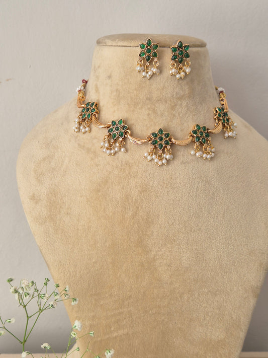 Modern Indian ethnic imitation jewelry set including a golden brass alloy floral-themed choker necklace embedded with green gemstones and white pearl drops, by naitri.in