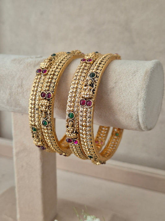 Four gold-plated bangles decorated with small clear stones and colorful red and green gemstone accents, by naitri.in