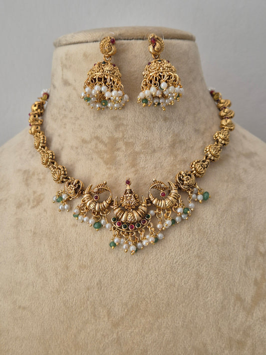 Gold-toned traditional Indian jewelry set featuring a jhumka earrings pair the pieces are decorated with white pearl-like beads, small green stones, and tiny red stones by naitri.in