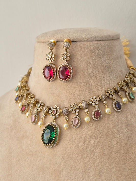 An ornate gold-toned traditional necklace set with matching earrings, the necklace features multiple oval and round gemstone settings in pink, green, purple, and blue, accented with small white faux pearls by naitri.in