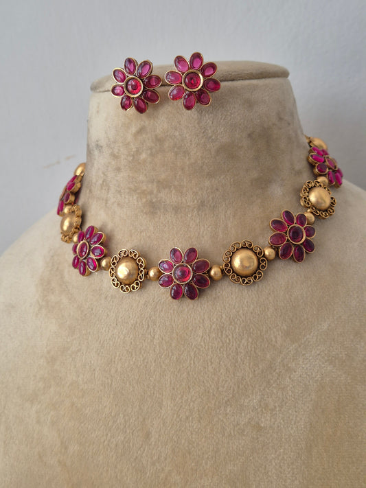 Modern Indian ethnic imitation jewelry set including a golden brass alloy choker necklace embedded with vibrant ruby-red stones in a floral pattern, by naitri.in