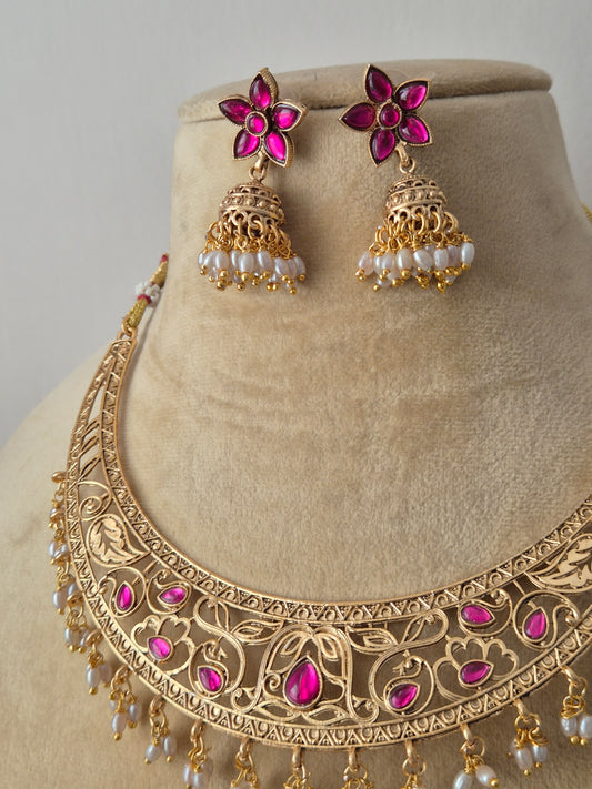 Traditional Indian antique-finish brass necklace set showcasing elaborate floral engravings, ruby-pink gemstone embellishments, and a structured collar silhouette with delicate pearl drops by naitri.in