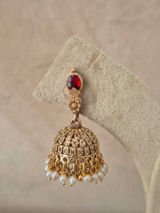 Close-up of Naitri Madhumita premium gold ethnic earrings showcasing traditional Indian temple jewelry craftsmanship with a ruby red stone accent and delicate pearl dangling beads