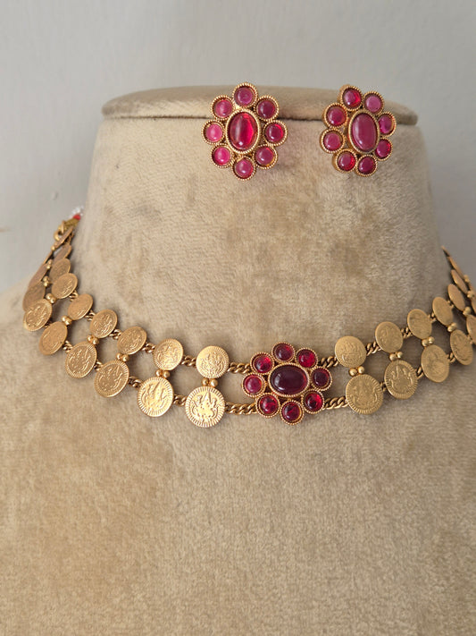 Gold-plated ethnic choker set composed of two rows of textured circular discs and a central ruby-pink gemstone flower, shown with matching flower stud earrings by naitri.in